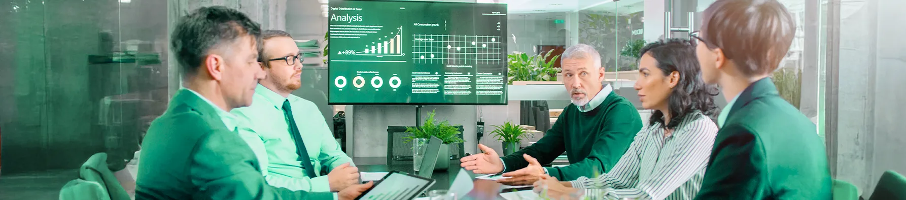 Uma equipe de executivos se reúne em uma sala de conferência moderna, com um gráfico de análise de dados exibido em uma tela grande. A discussão sugere o planejamento estratégico, essencial para manter a resiliência empresarial e responder a desafios do mercado.
