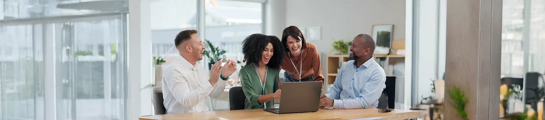 Quatro pessoas sorridentes em um escritório usam notebook para realizar a assinatura digital para assembleias e associações.